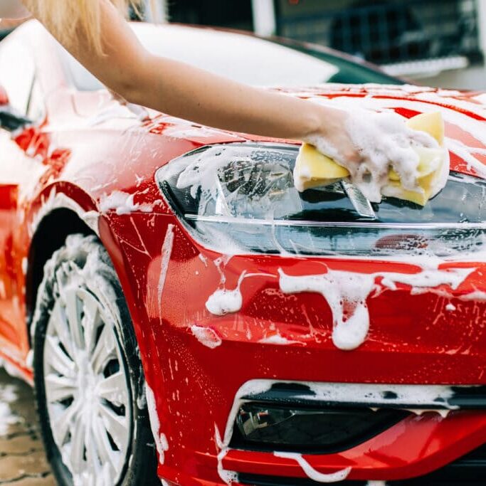 Young woman washing her car with sponge.